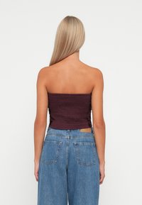 Burgundy strapless top with smocked texture, paired with light blue high-waisted denim jeans featuring back pockets and a tan leather label.
