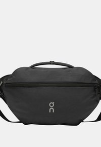 Kompakti musta vyötärötasku etuvetoketjulla, punottu kahva, jossa on "SWISS SEIL" -merkintä, ja heijastava "on"-logo etuosassa keskellä.