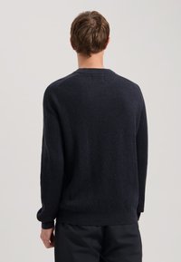 Pulover tricotat navy cu textură canalată, guler rotund și mâneci lungi. Prezintă un brâu și mansete ajustate. Design minimalist.
