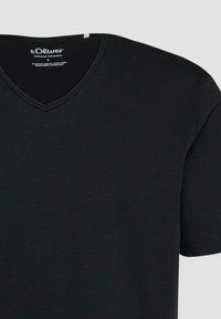 T-shirt noir manches courtes à col en V avec étiquette s.Oliver Clothing Company à l’intérieur du col, taille large, sur fond gris neutre.