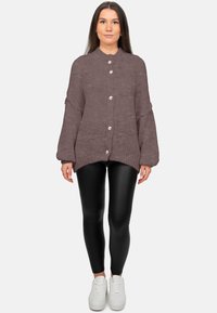 Cardigan violet tricoté avec un col arrondi, une fermeture à boutons sur le devant, et des manches surdimensionnées, associé à un legging noir et des baskets blanches.