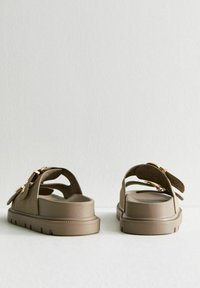 Bruna sandaler med en texturerad yta, två justerbara remmar och detaljer i guldfärg. Tjock sula med urfräst dekor. Bakifrån.