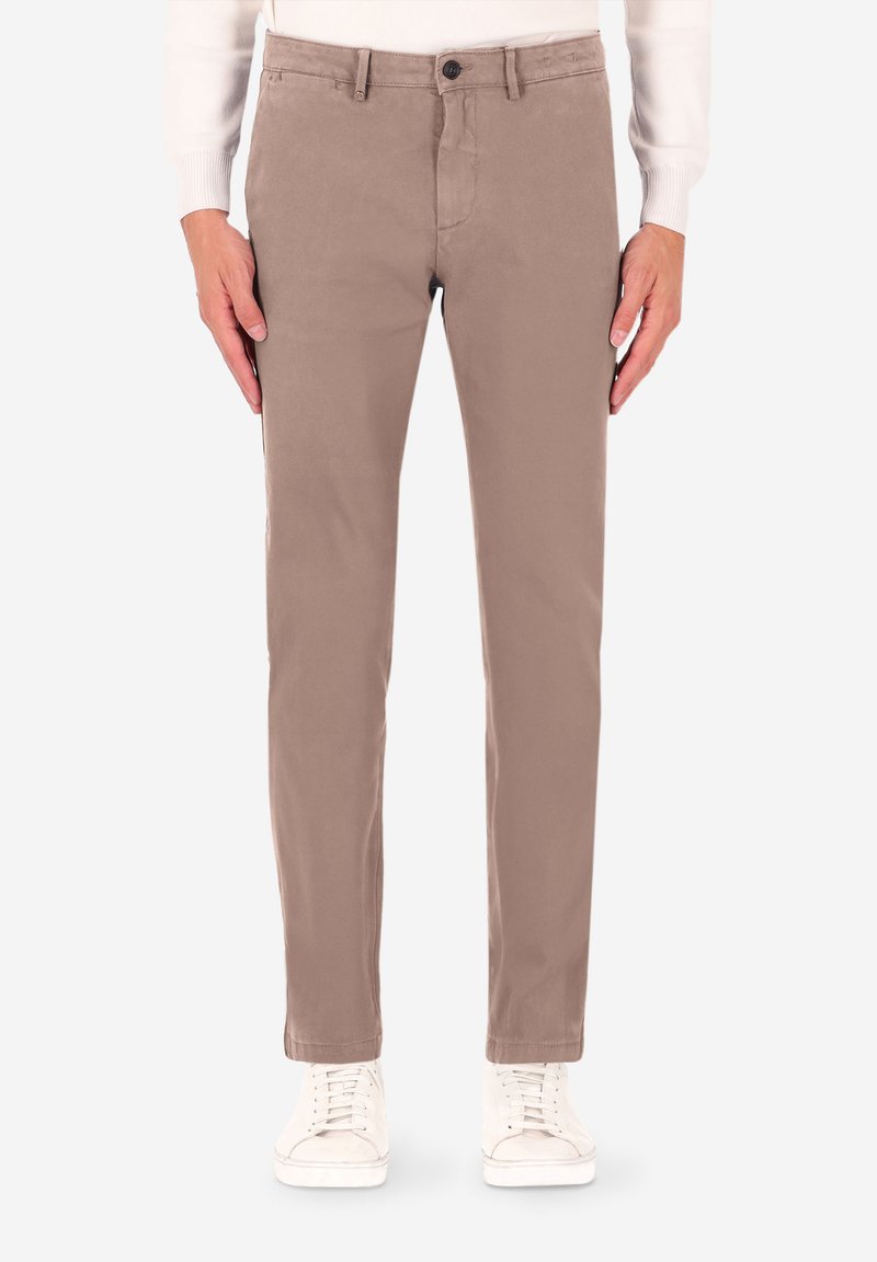 I pantaloni chino beige hanno una vestibilità slim con una texture liscia, chiusura con bottoni e tasche laterali, abbinati a sneakers bianche.
