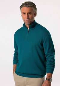 Teal stickad tröja med halvdragkedja, ribbade ärmslut och nederkant. Slät textur med en avslappnad passform, i kombination med ljusa byxor.