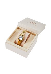 Montre rectangulaire dorée avec un cadran blanc et des chiffres romains noirs sur un bracelet en métal à maillons, présentée dans une boîte rembourrée beige.