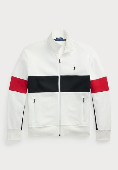 Λευκό φούτερ με φερμουάρ και όρθιο γιακά. Διαθέτει κόκκινες και μαύρες οριζόντιες ρίγες στο στήθος και τα μανίκια. Δύο πλευρικές τσέπες με φερμουάρ.