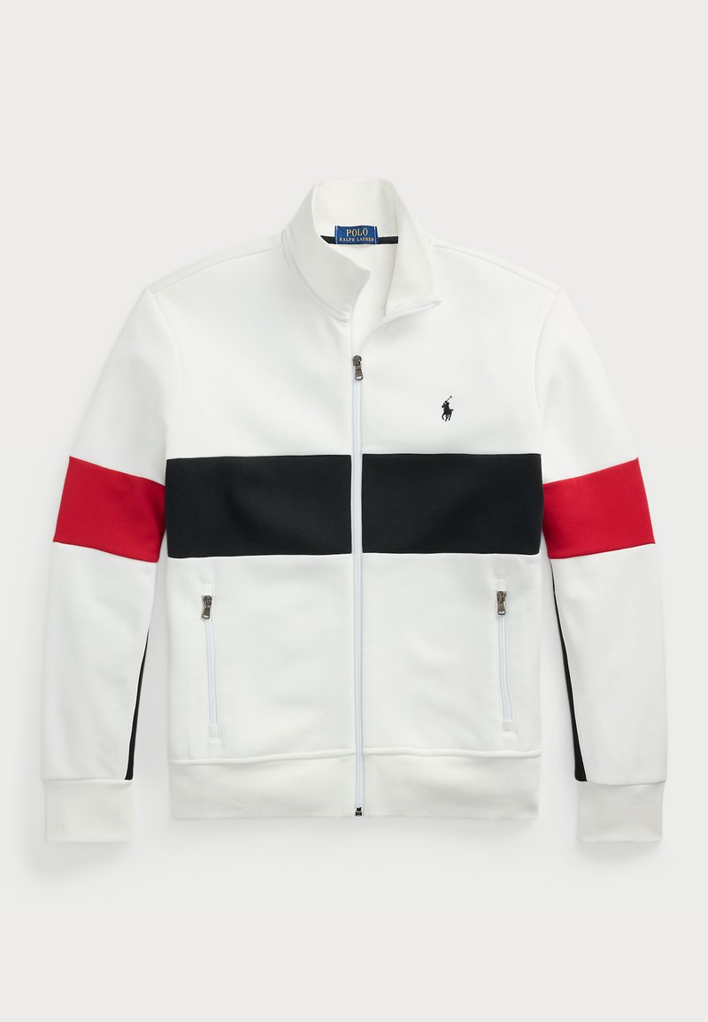 Valkoinen vetoketjullinen takki, jossa on pystykaulus. Rintakehässä ja hihoissa on punaisia ja mustia vaakasuoria raitoja. Kaksi sivuläppävetoketjupussukkaa.