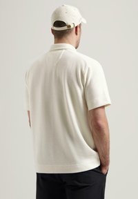 Kortermet polo skjorte i off-white, teksturert strikket stoff. Har krage og sidesplitter, kombinert med en matchende caps.