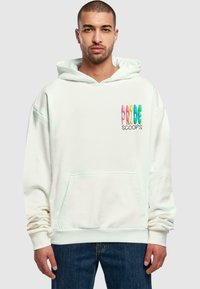 Hvid hættebluse med en frontlomme og snoretræk i hætten. "PRIDE" i farverig tekst med "SCOOPS" nedenunder. Blød tekstur, oversized design.