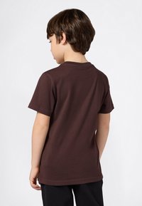 T-shirt in cotone marrone con maniche corte e scollo rotondo, vista da dietro. Design semplice, texture uniforme, nessun motivo o dettaglio visibile.