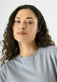 Graues T-Shirt mit Rundhalsausschnitt und einem dezenten, gestickten Blumenlogo auf der linken Brust. Weicher Stoff mit glatter Textur.