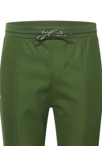 Pantalon de sport vert avec une surface texturée, taille élastique et fermeture à cordon. Présente des détails de coutures subtils et des poches.