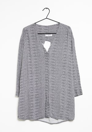 Grå tekstureret top med V-hals, lange ærmer og en høj-lav søm. Har et subtilt prikket mønster og et plejeetiket vedhæftet.