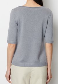 Jasnoszary sweter z dzianiny z krótkimi rękawami i prążkowanym wykończeniem. Gładka tekstura i luźny krój, z szerokim dekoltem i bocznymi rozcięciami.