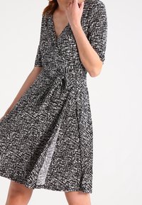 Svart-och-vit omlottklänning med korta ärmar, texturerad tyg med en geometrisk mönster och en åtsittande midja med en utsvängd kjol.
