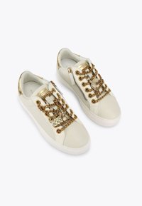Sneakers bianchi in pelle con hardware dorato, dettagli a catena e zip laterale. Texture liscia e design low-top.