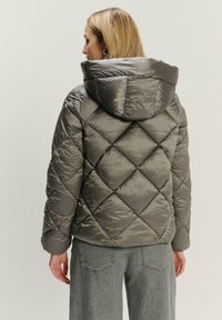 Prešívaná puffer bunda v metalickosivej farbe so kapucňou, diamantovým vzorom a lesklým nylonom. Mäkka textúra a objemový tvar.