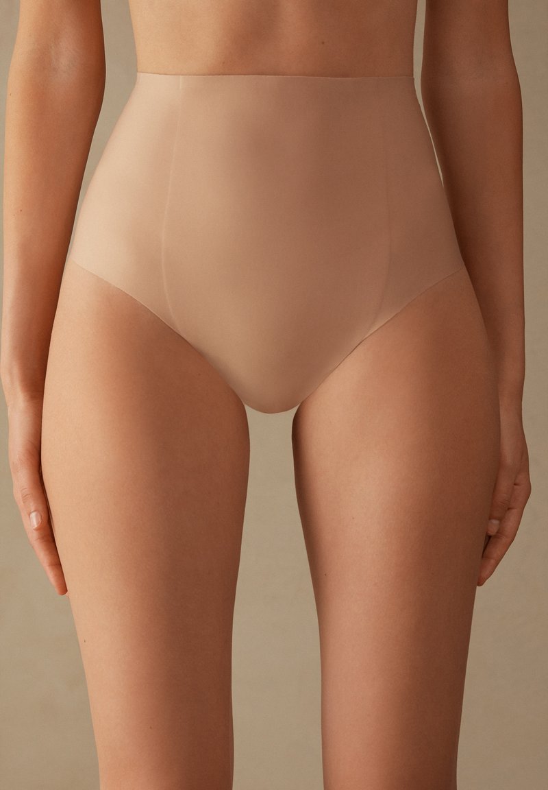Nude high-waisted ondergoed gemaakt van gladde, rekbare stof. Beschikt over naadloze randen en een minimalistisch ontwerp voor een gestroomlijnde uitstraling.