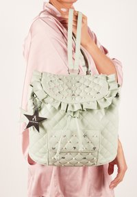 Zaino verde menta trapuntato con patta arricciata, ciondolo a forma di stella e dettagli in perline. Presenta spallacci regolabili e una tasca anteriore.