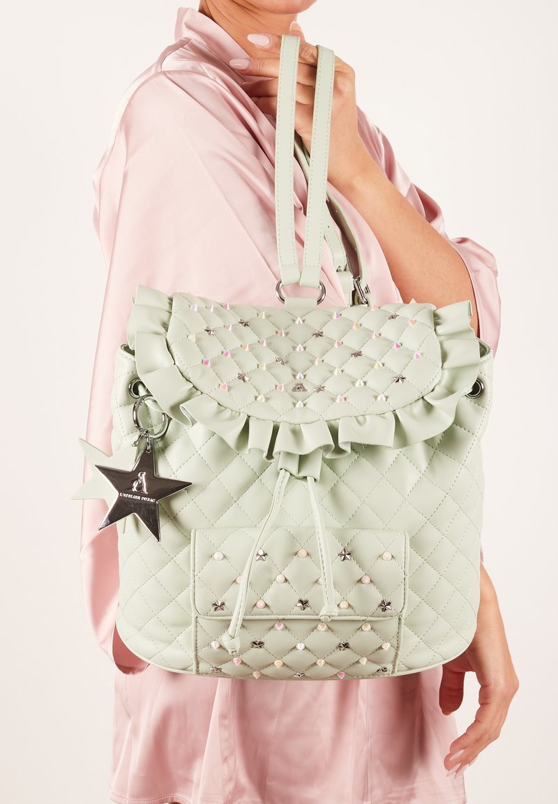 Zaino verde menta trapuntato con patta arricciata, ciondolo a forma di stella e dettagli in perline. Presenta spallacci regolabili e una tasca anteriore.