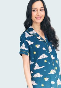 Conjunto de pijama de manga corta en tejido azul con nubes blancas, estrellas y conejos. Con un contrastante ribete amarillo en el cuello y las mangas.