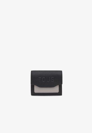 Billetera de cuero negro con un panel de acento gris, con el logo "TOUS" en relieve en la parte frontal. Forma rectangular compacta, superficie texturizada.