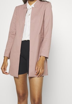 Blush pink blazer with a collar, long sleeves, open front, and two side pockets, worn over a white shirt and black shorts.