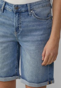 Shorts de mezclilla en azul claro, con un diseño de cinco bolsillos, un botón en la cintura, puños enrollados y detalles de costura sutiles.