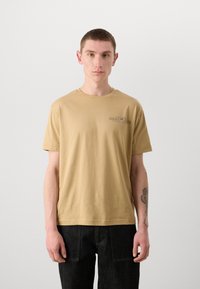 Kortärmad t-shirt med rundad halsringning i beige bomull, med en liten GANT-logotyp i svart på vänster bröst. Enkel, rak skärning.