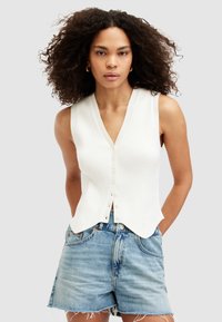 Vit ribbad ärmlös topp med V-ringning och knappknäppning; har en figurnära design och något utsvängd nederkant, tillsammans med denimshorts.