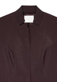 Dunkelbraunes Nahaufnahme eines maßgeschneiderten Blazerkragens mit einem aufgeschlitzten Revers und subtilen Nahtdetails auf der Vorderseite.