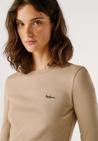 Beež ribast pikkade varrukatega topp ümmarguse kaelusega ja musta "Pepe Jeans" logo aktsendiga vasakul rinnal. Pehme tekstuur, liibuv disain.