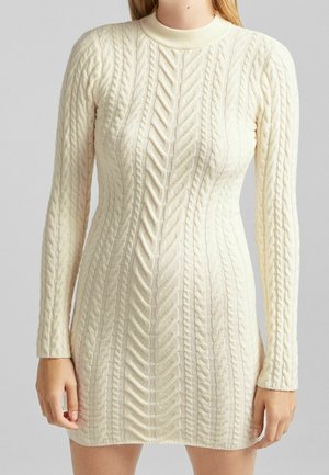 Robe pull ajustée à manches longues en maille torsadée couleur crème, avec un col rond haut et des motifs texturés.
