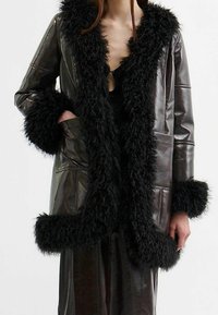 Bruin leren jas met faux fur-kraag, een diepe V-hals, wijde manchetten en zijzakken, met een glanzende textuur en luxueuze ontwerpelementen.