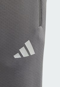 Grå sportbyxor i stretchmaterial. Har en liten reflekterande vit Adidas-logotyp på låret och en sidoficka.