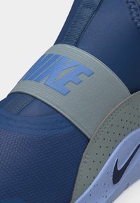 Modrá teniska Nike so sivým elastickým pásikom cez hornú časť a perforovanou sivou bočnou časťou, s čiernou značkou Nike na svetlomodrej podrážke.