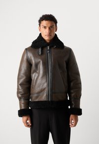 Giubbotto bomber in pelle marrone con colletto e polsini in shearling nero. Presenta una chiusura con zip, tasche laterali e bordi a contrasto.