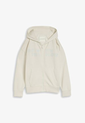 Svetlo bež pulover s kapuco na zadrgo, sprednjimi žepi in napisom "SPREJMI TOK" čez prsni del v ujemajoči se svetli barvi.