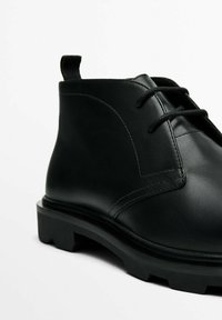 Czarne skórzane botki za kostkę o gładkim wykończeniu, z okrągłym noskiem, sznurowanym zapięciem oraz teksturowaną czarną gumową podeszwą.