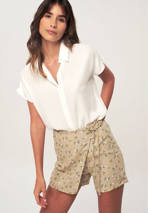 White short-sleeved blouse with a button-down front, paired with beige shorts featuring a floral pattern in green and yellow, tied at the waist.