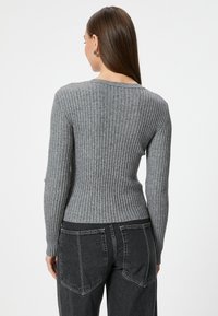 Grijze geribbelde trui met lange mouwen en een aansluitende pasvorm, gecombineerd met zwarte high-waisted jeans met opgestikte zakken.
