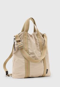 Bolso de tela beige con una superficie texturada, con costuras rojas en contraste, doble asa superior y una correa de hombro ajustable.