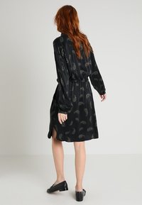 Svart sident klänning med långa ärmar, elastisk midja och sidoklipp. Har ett subtilt mönster med ljusa inslag genom hela.