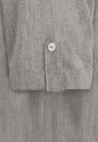 Graues Leinenhemd mit Knopfverschluss, sichtbarer Textur und Manschettendetails mit gesticktem Saum. Weicher, atmungsaktiver Stoff.