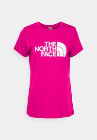 Camiseta rosa de algodón con mangas cortas, con un logo blanco de "THE NORTH FACE" y un acento curvado en el lado izquierdo. Textura lisa.