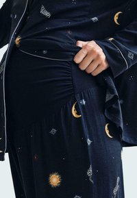 Conjunto de pijama azul marino con estampados celestiales, que presenta patrones de sol, luna y estrellas. Tela suave con corte relajado y detalles de fruncido en la cintura.