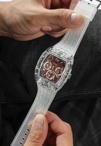 Clear plastic watch with a transparent strap, featuring a red and black patterned dial, three sub-dials, and silver-tone accents.