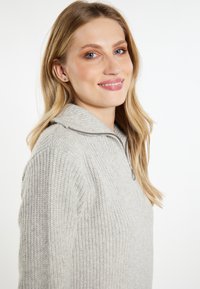 Lichtgrijze trui met geribbelde textuur, half-zip kraag en een relaxte pasvorm. Beschikt over zacht materiaal en een casual ontwerp.