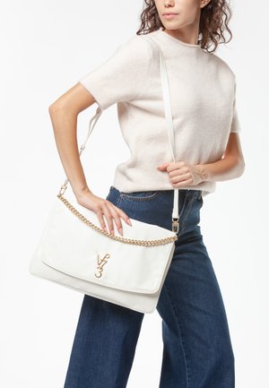 Mujer con suéter crema de manga corta y jeans azules sostiene un bolso de hombro blanco de cuero con cadena dorada y logo V 3.