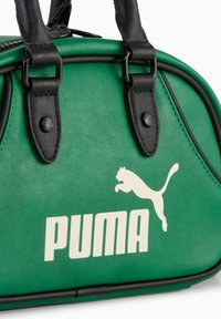 Sac à main synthétique vert avec des poignées en cuir noir, arborant un logo Puma blanc prominent et un design arrondi élégant.